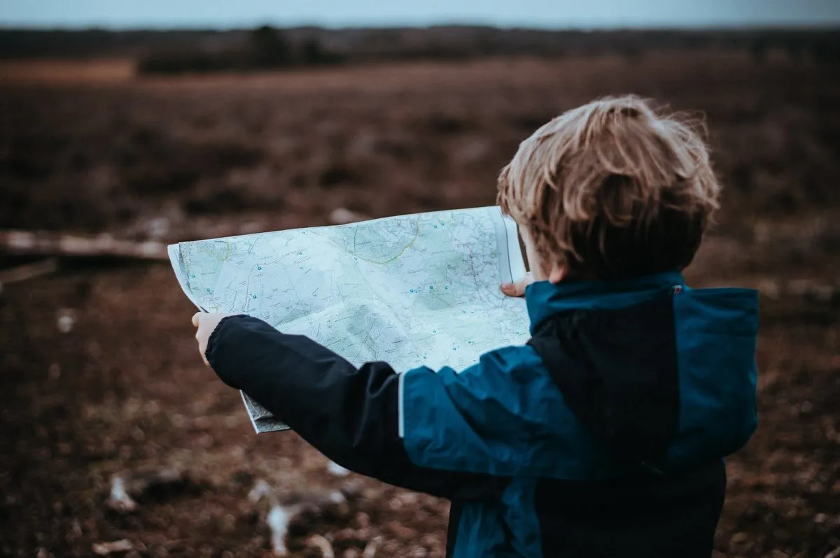 A child holding up a large map in an open landscape